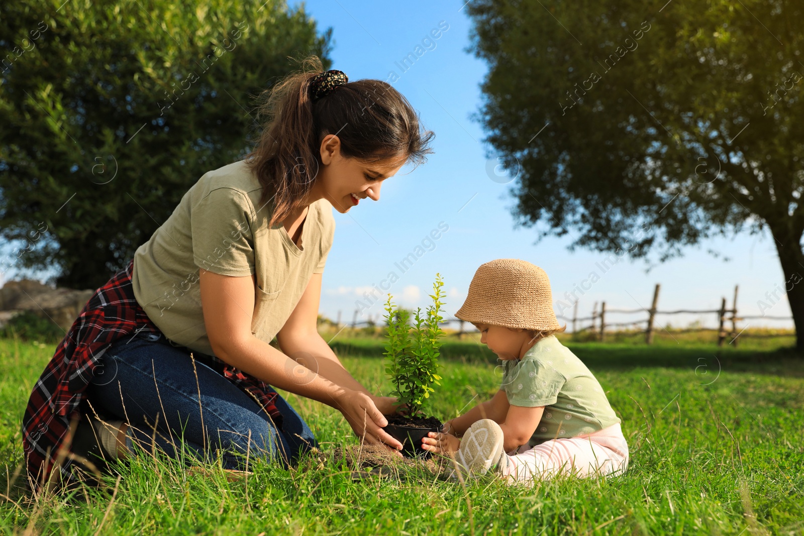 Photo of Mother and her baby daughter planting tree together in garden