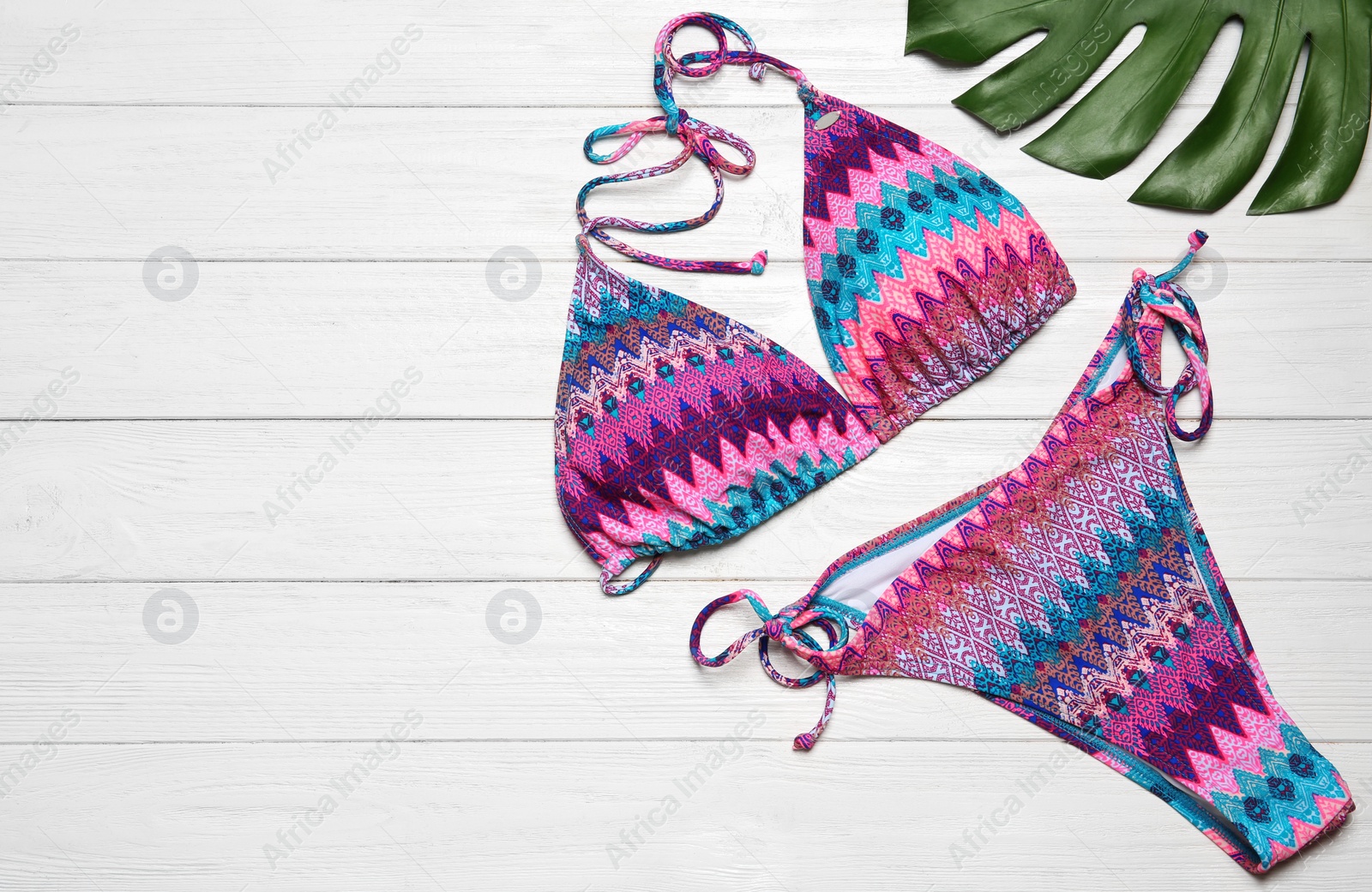 Photo of Stylish bikini, tropical leaf and space for text on wooden background, flat lay