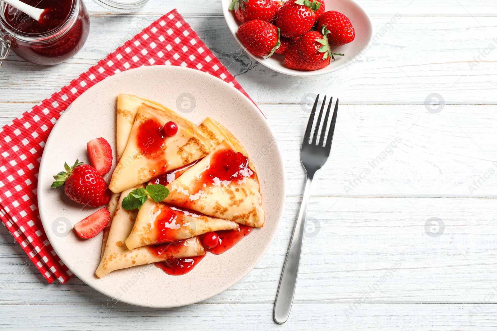 Photo of Delicious thin pancakes with strawberries and jam on white wooden table, flat lay