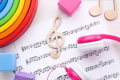 Photo of Notes, music sheets, headphones and toys on white wooden table, flat lay. Baby song concept