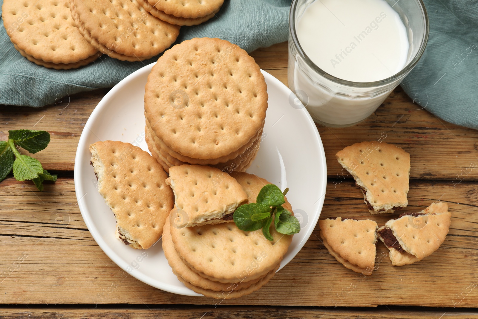 Photo of Tasty sandwich cookies and glass of milk on wooden table, flat lay