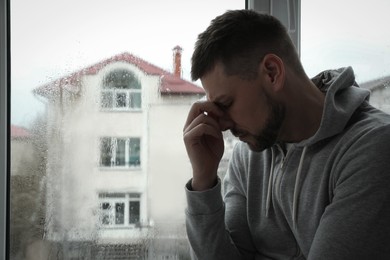 Photo of Depressed man near window at home. Space for text