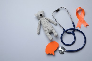 Photo of Orange ribbon, toy bear, stethoscope and paper brain cutout on light grey background, flat lay with space for text. Multiple sclerosis awareness
