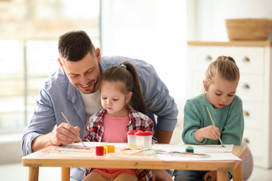 Photo of Father and daughters painting at table indoors. Playing with children