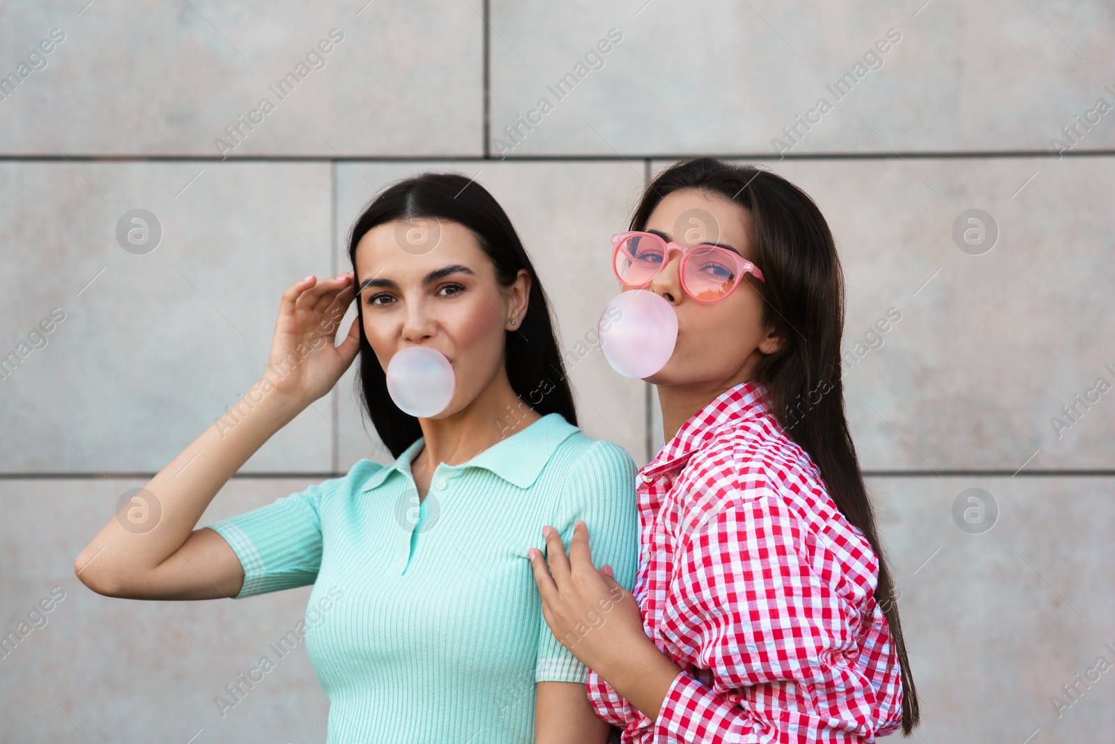 Photo of Beautiful women blowing gums near wall outdoors