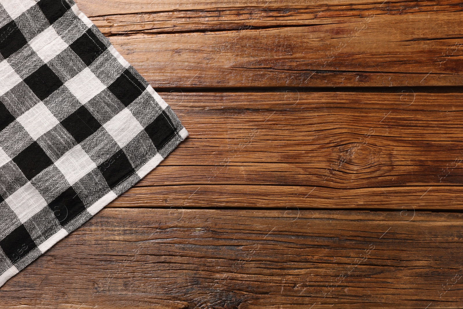 Photo of Black checkered tablecloth on wooden table, top view. Space for text