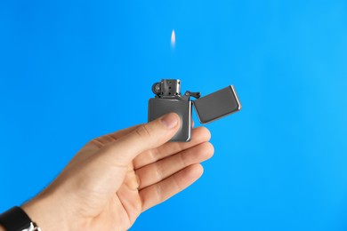 Photo of Man holding lighter with burning flame on light blue background, closeup. Space for text