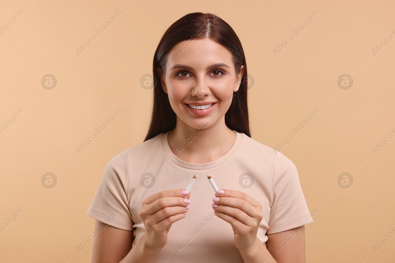 Photo of Stop smoking concept. Happy young woman holding pieces of broken cigarette on light brown background