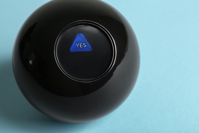 Photo of Magic eight ball with prediction Yes on light blue background, closeup. Space for text