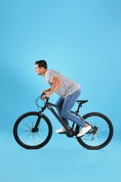 Handsome young man with modern bicycle on light blue background