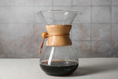Glass chemex coffeemaker with tasty drip coffee on white table