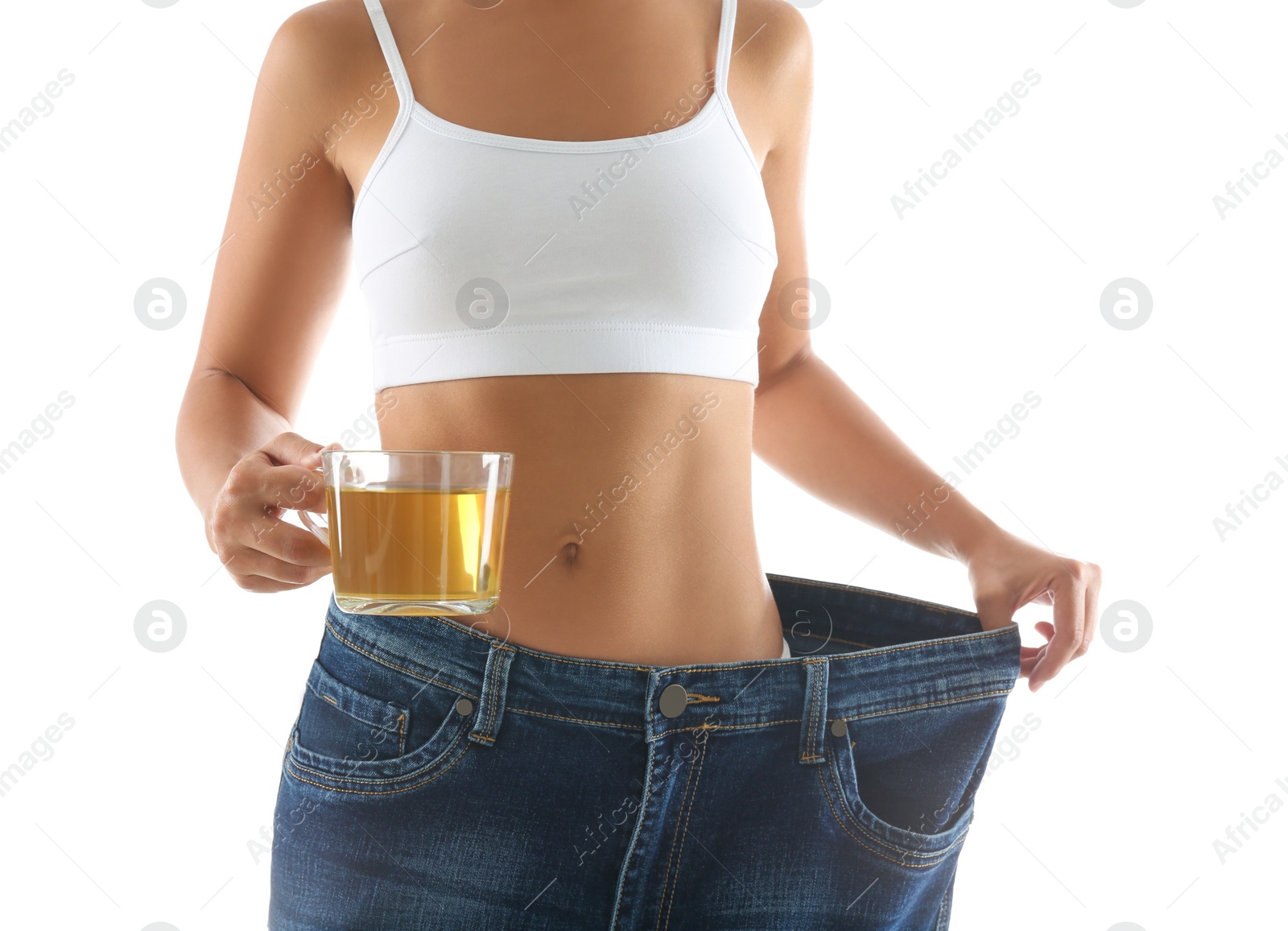 Photo of Young woman in old big jeans with cup of tea showing her diet results on white background, closeup