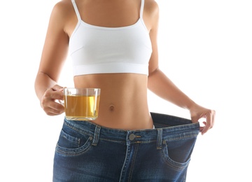 Photo of Young woman in old big jeans with cup of tea showing her diet results on white background, closeup