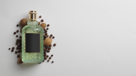 Bottle of perfume surrounded by allspice and nutmegs on white background, top view. Space for text