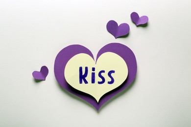Paper hearts and one with word Kiss on beige background, flat lay