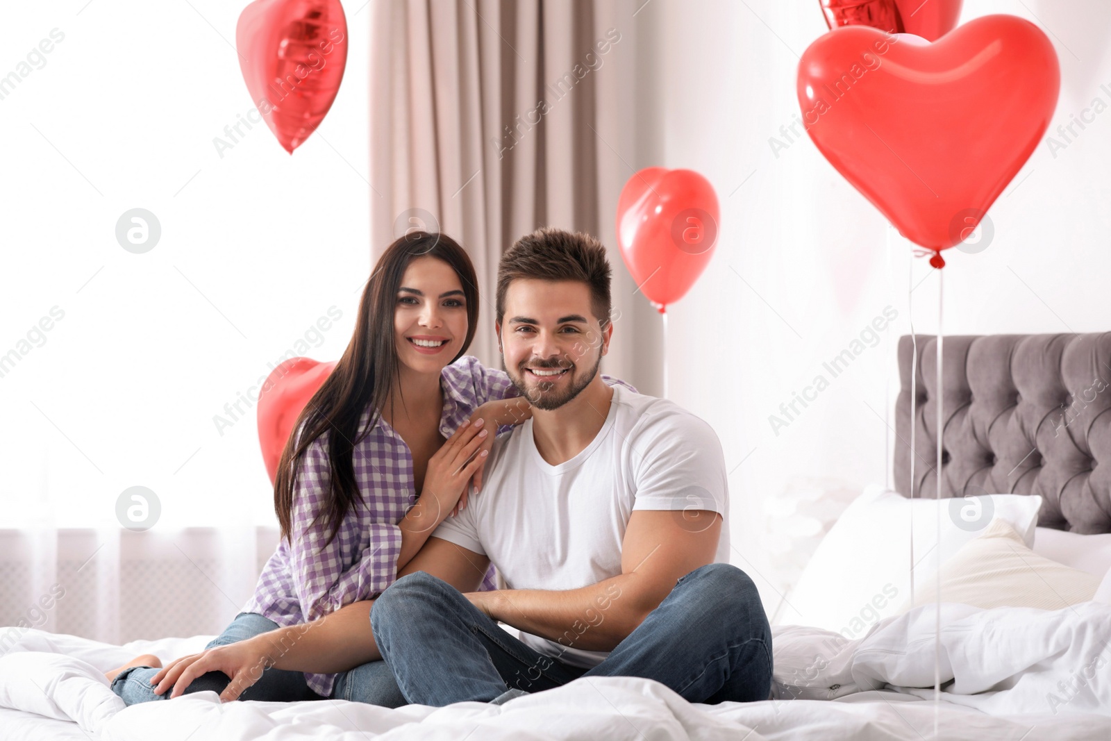 Photo of Lovely young couple in bedroom decorated with heart shaped balloons. Valentine's day celebration