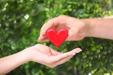 Photo of Man giving red heart to woman on blurred green background, closeup. Donation concept