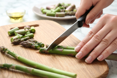 Photo of Woman cutting asparagus on wooden board, closeup