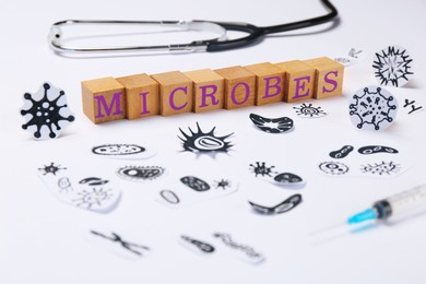 Photo of Word Microbes made with wooden cubes, pictures, syringe and stethoscope on white background