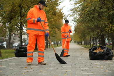 Street cleaners sweeping fallen leaves outdoors on autumn day