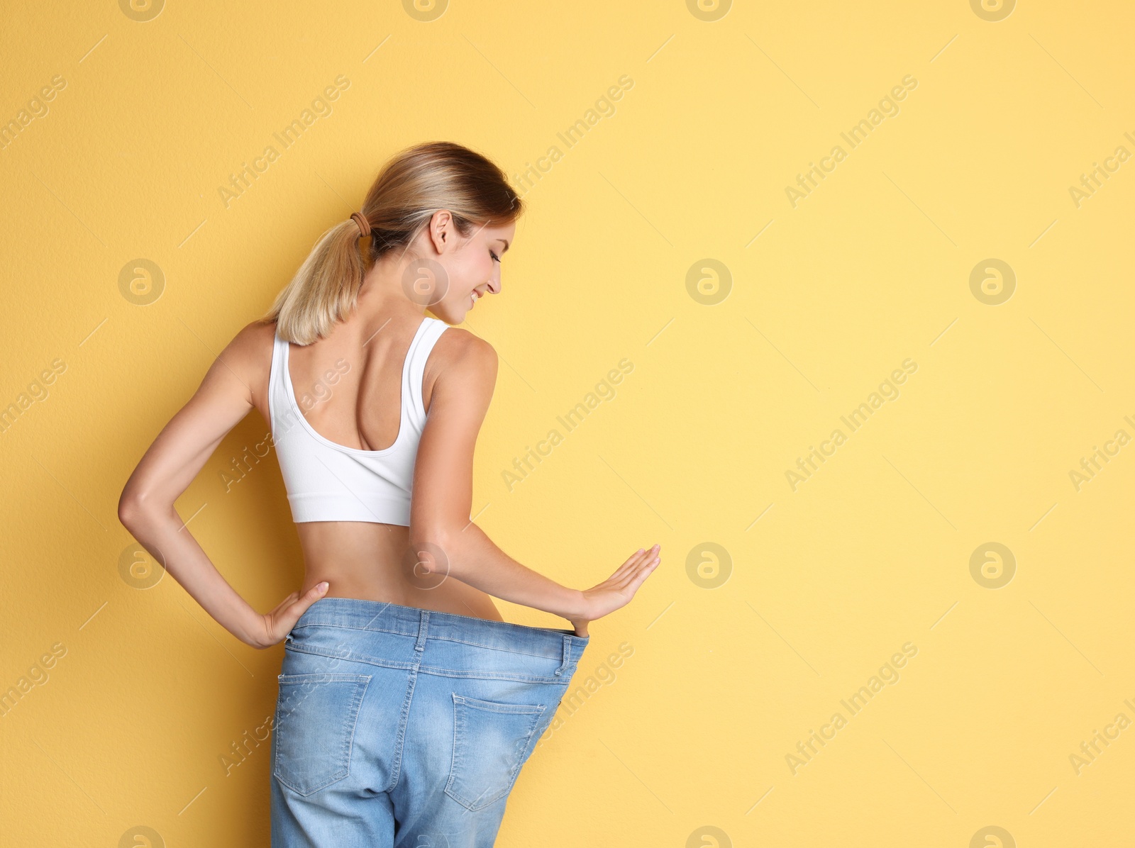 Photo of Young slim woman in old big jeans showing her diet results on color background