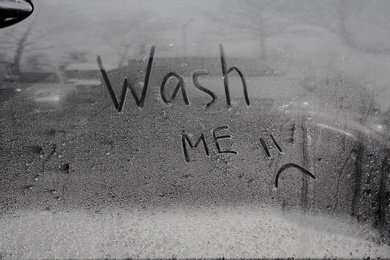 Photo of Inscription WASH ME and sad smiley on car door, closeup