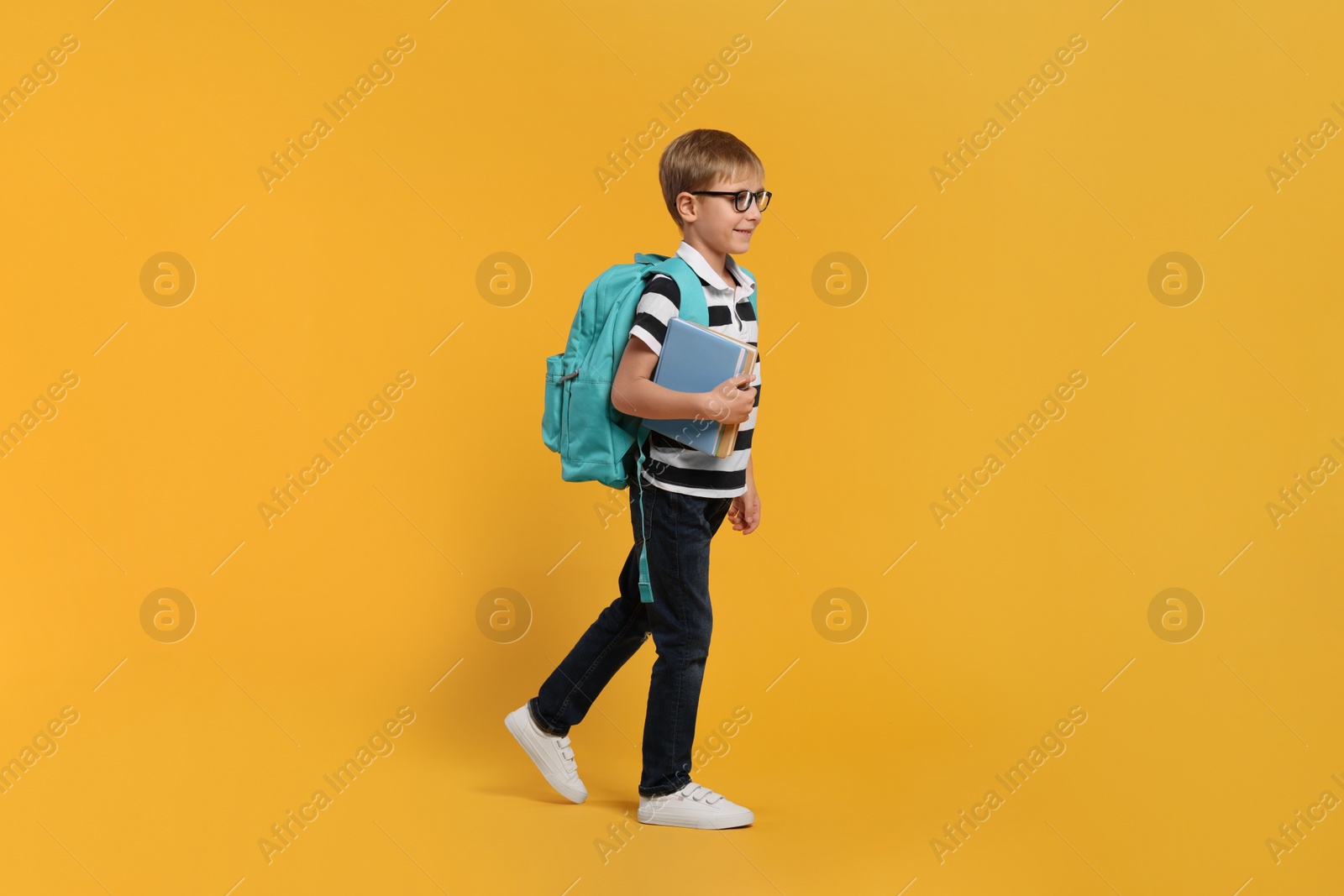 Photo of Happy schoolboy in glasses with backpack and books on orange background