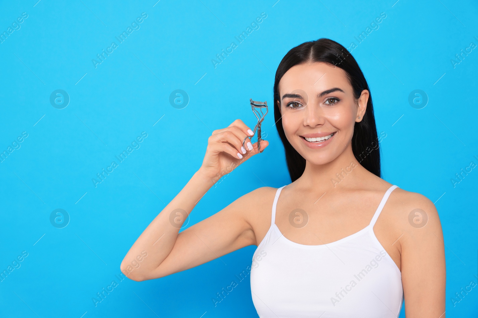 Photo of Beautiful young woman with eyelash curler on light blue background, space for text