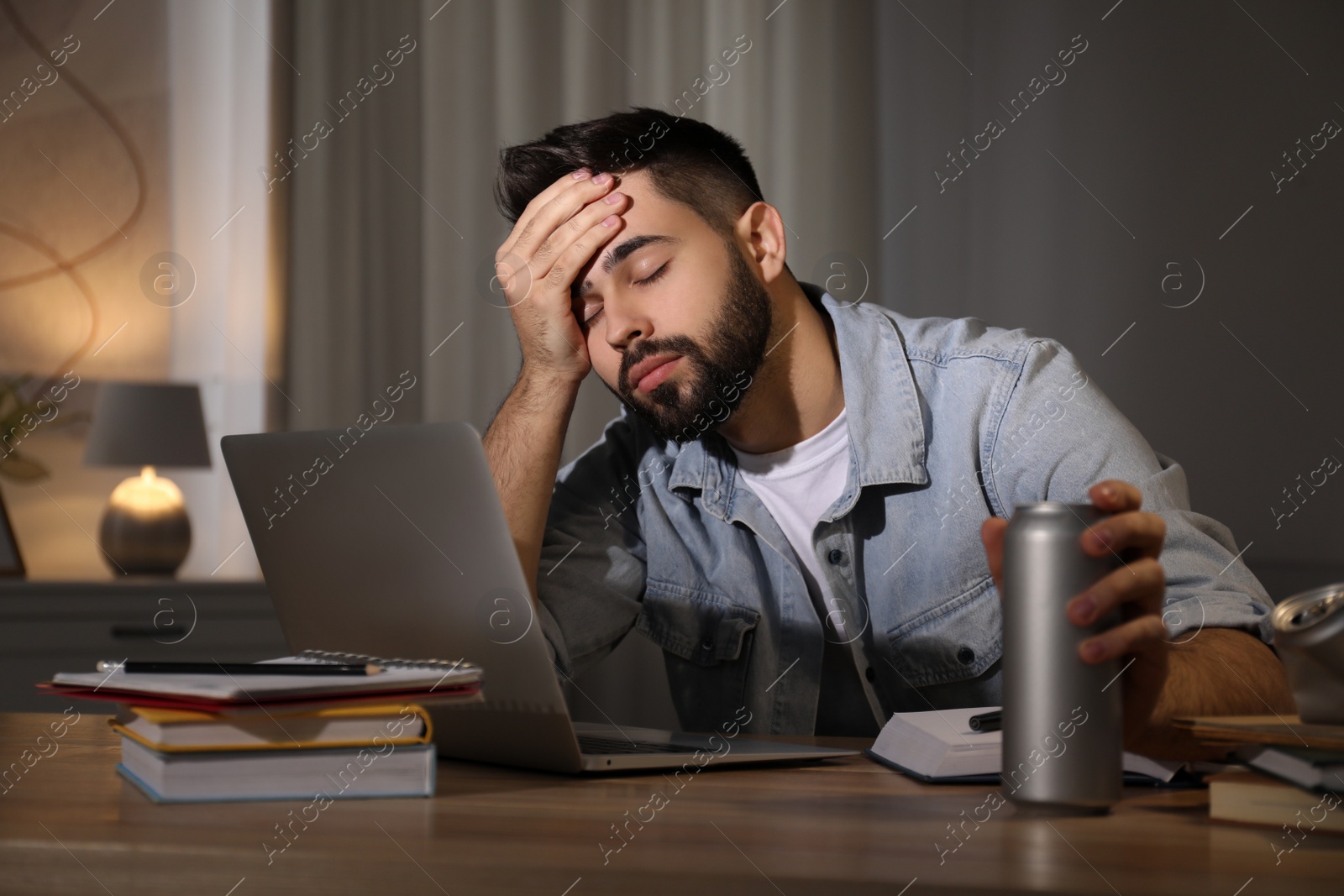 Photo of Tired young man with energy drink studying at home