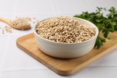 Photo of Dry pearl barley in bowl on white tiled table, closeup