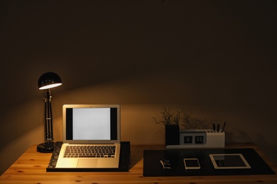 Photo of Dark room interior with laptop and devices on table. Space for text