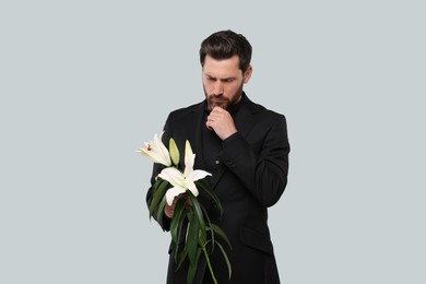 Photo of Sad man with white lilies on light grey background. Funeral ceremony