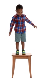 Photo of Little African-American boy standing on stool on white background. Danger at home