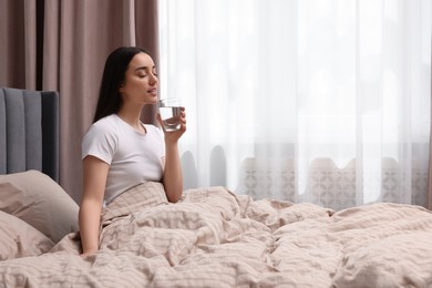 Photo of Beautiful woman with glass of water on bed at home, space for text. Lazy morning