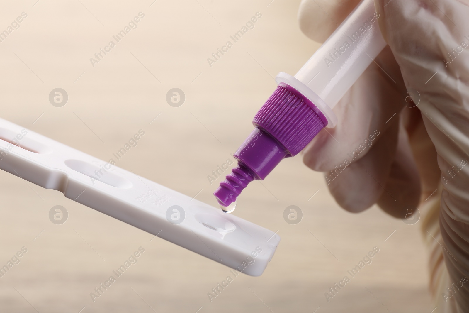 Photo of Doctor dropping buffer solution onto disposable express test cassette against blurred background, closeup
