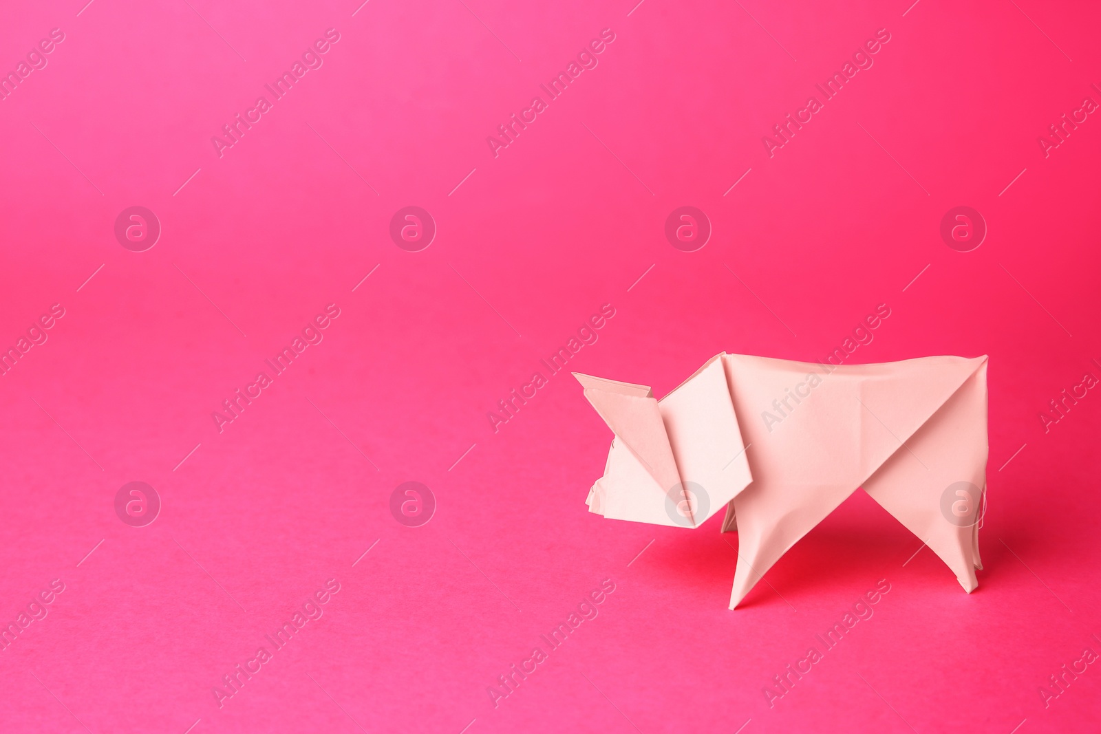 Photo of Origami art. Handmade bright paper pig on pink background, space for text