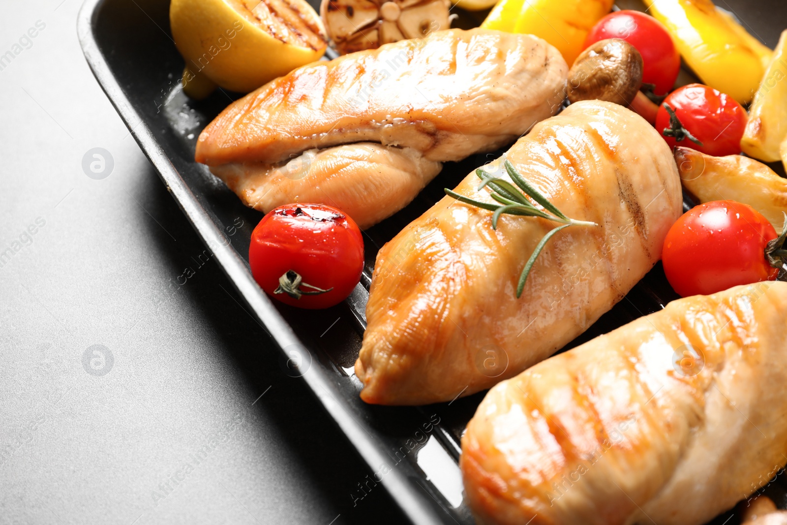 Photo of Grill pan with fried chicken breasts and garnish on grey background, closeup