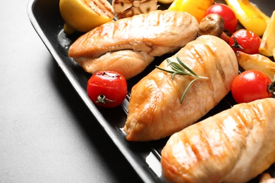 Grill pan with fried chicken breasts and garnish on grey background, closeup