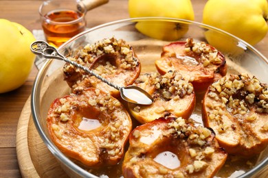 Photo of Tasty baked quinces with walnuts and honey in bowl on table, closeup