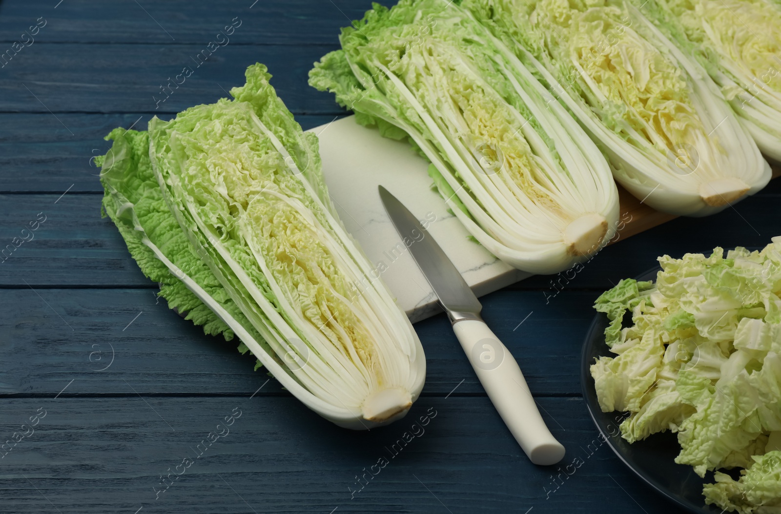 Photo of Cut fresh ripe Chinese cabbages on blue wooden table