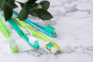 Photo of Colorful plastic toothbrushes and plant twig on white marble table, closeup. Space for text