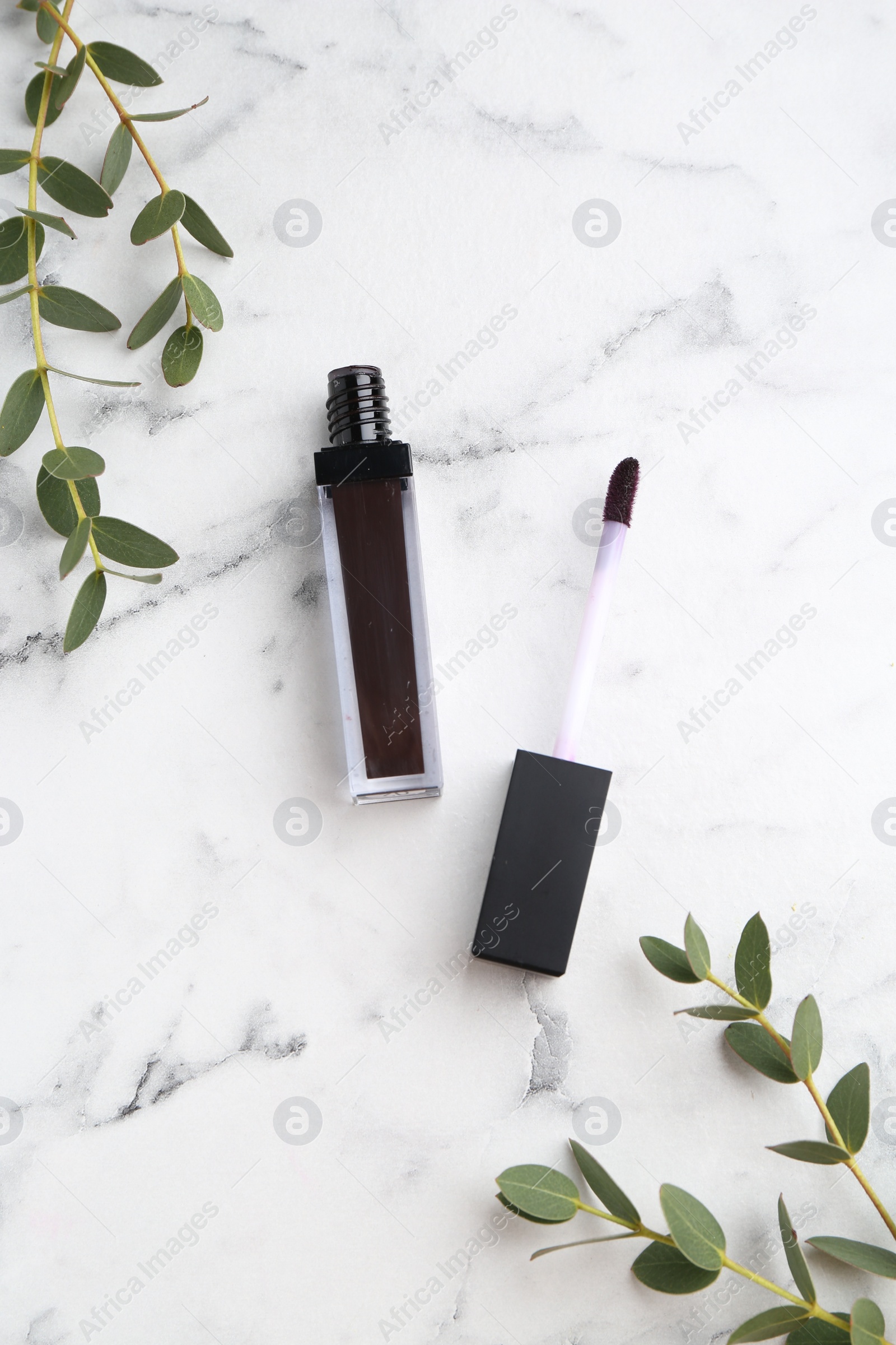 Photo of Purple lip gloss, applicator and green leaves on white marble table, flat lay