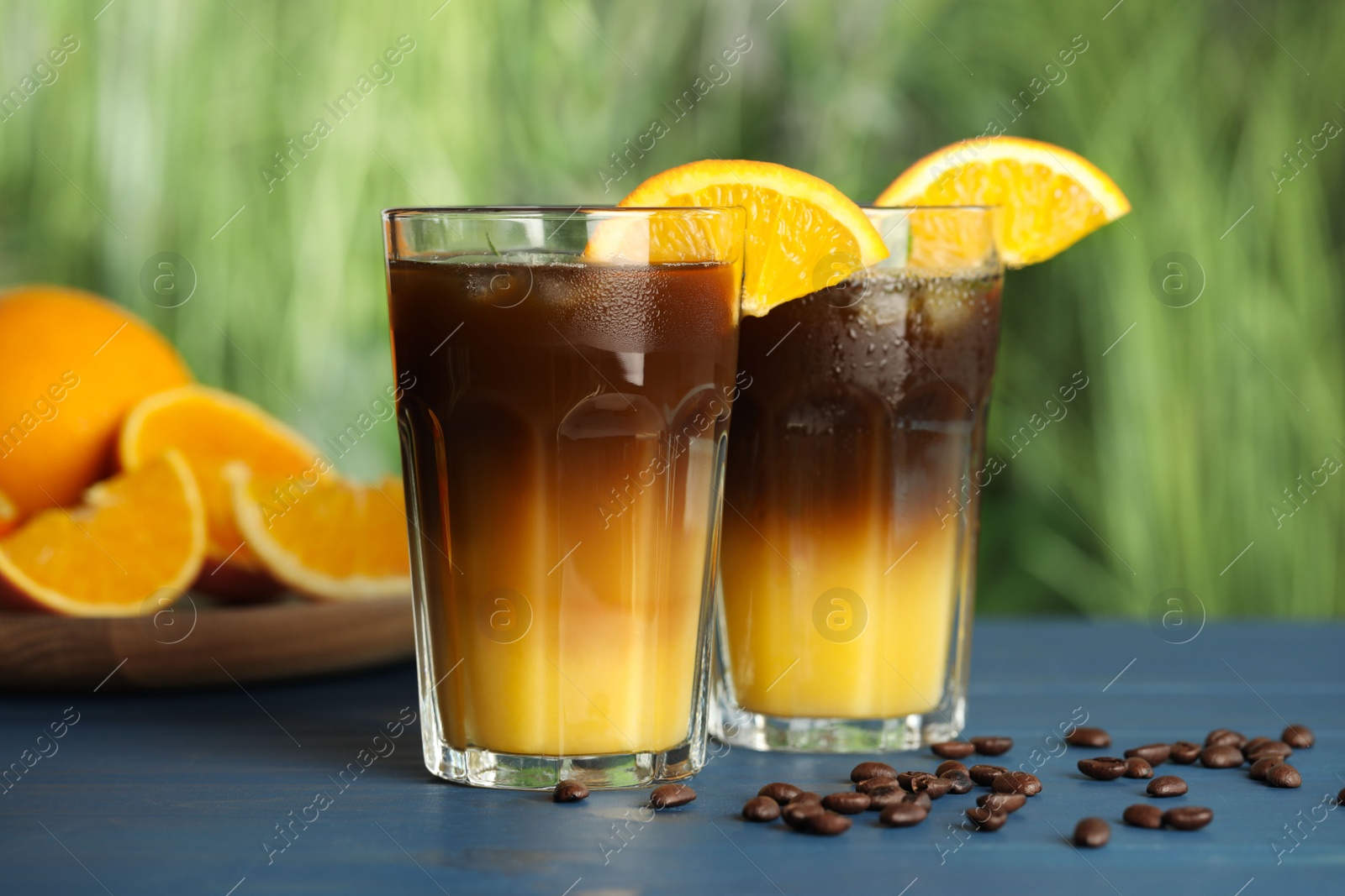 Photo of Tasty refreshing drink with coffee and orange juice on blue wooden table against blurred background