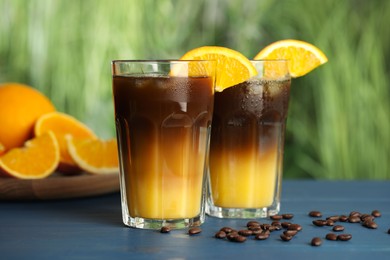 Tasty refreshing drink with coffee and orange juice on blue wooden table against blurred background