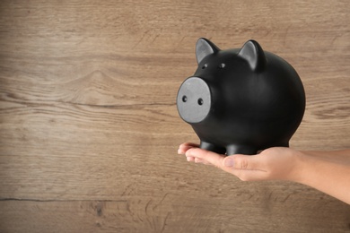 Photo of Woman holding piggy bank on wooden background, closeup view. Space for text