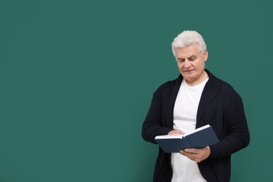 Portrait of senior teacher with book at green chalkboard, space for text