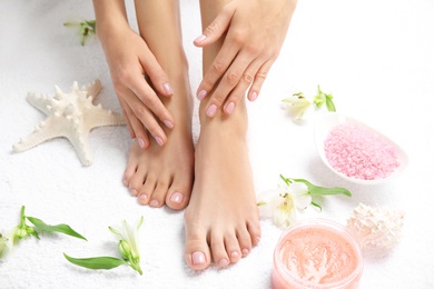 Photo of Cosmetic, flowers and woman touching her smooth feet on white towel, closeup. Spa treatment