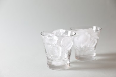 Photo of Ice cubes in glasses on grey background. Space for text