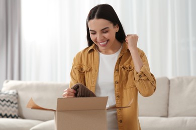 Emotional young woman opening parcel at home. Internet shopping