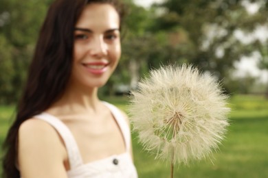 Beautiful young woman with large dandelion in park, focus on flower. Allergy free concept